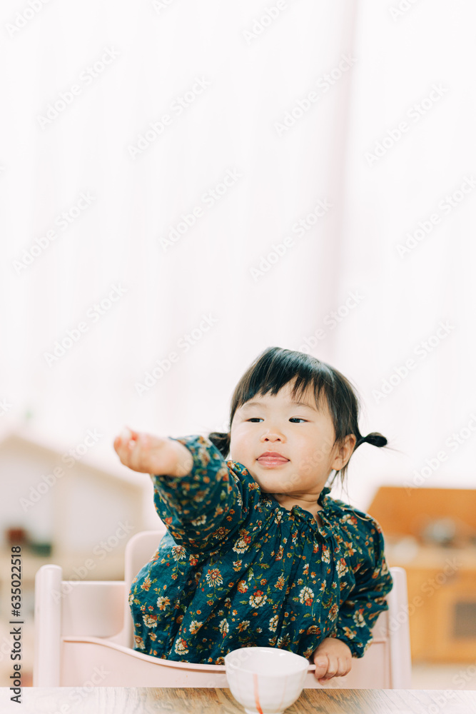 秋の午後、家で椅子に座って腕を伸ばしおやつを見つめるアジア人の子供 秋の午後、家で椅子に座って腕を伸ばしおやつを見つめるアジア人の子供