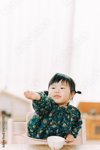 秋の午後、家で椅子に座って腕を伸ばしおやつを見つめるアジア人の子供