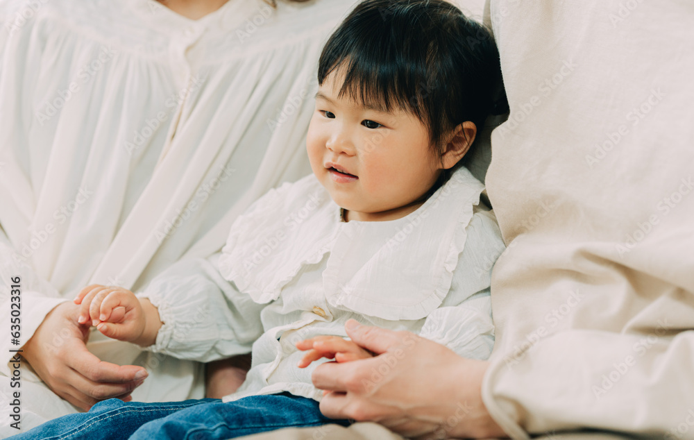 春の朝、両親に挟まれて座り母親の指を掴むアジア人の子ども