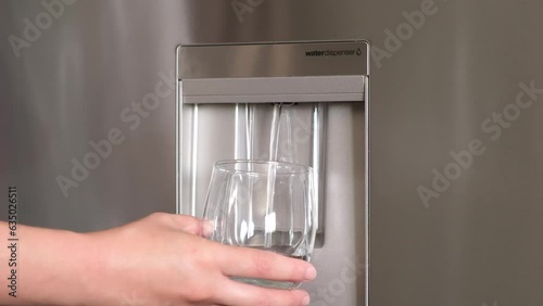 Hand-pushing cup for pure water freshness for a healthy lifestyle. Modern cooler water dispenser in a residential kitchen refrigerator. Water filtration machine.