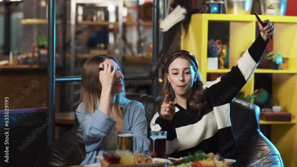 Two girls are sitting in a restaurant, they are in a good mood, trying to take a selfie, and having a fun time together. Two girls are sitting in a restaurant, they are in a good mood, trying to take a selfie, and having a fun time together.