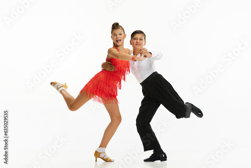 Emotional, delightful kids, boy and girl in beautiful stage costumes dancing against white studio background. Concept of childhood, hobby, active lifestyle, performance, art, fashion