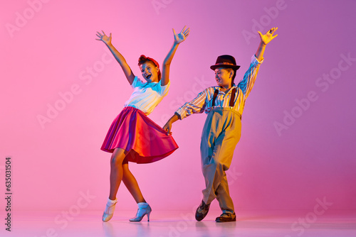 Canvas Print Emotional and stylish children, boy and girl in retro clothes dancing lindy hop against pink studio background in neon light