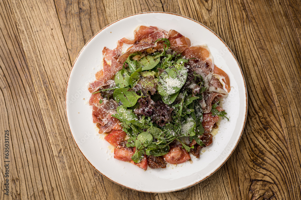 delicious salad with parmesan, jamon, tomatoes on a white plate delicious salad with parmesan, jamon, tomatoes on a white plate