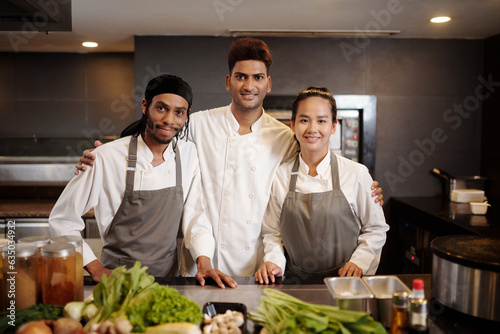 Portrait of proud restaurant chef and his team standing at table with fresh ingredients