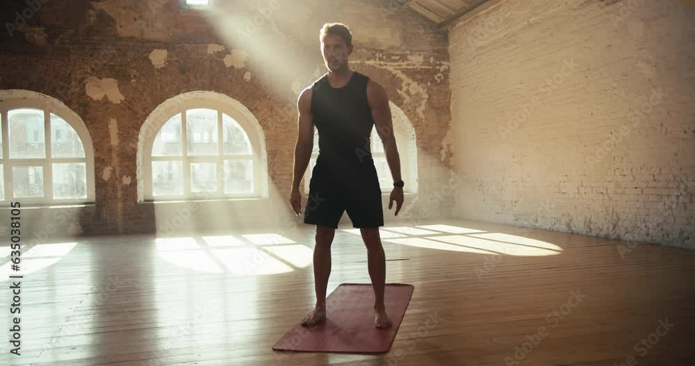 A man does exercises and squats in a sunny gym on a special carpet for sports. Doing sports in the sunny gym workout in the morning A man does exercises and squats in a sunny gym on a special carpet for sports. Doing sports in the sunny gym workout in the morning