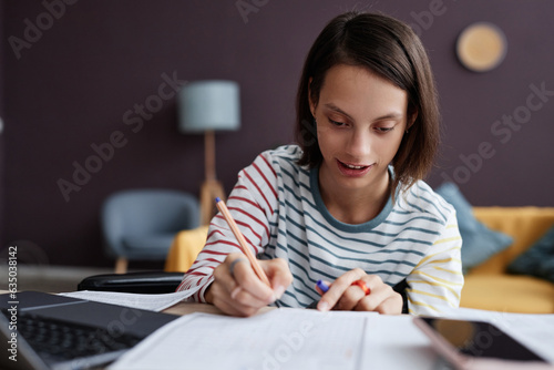 Close up portrait of teenage girl with disability doing homework while studying from home, copy space photo
