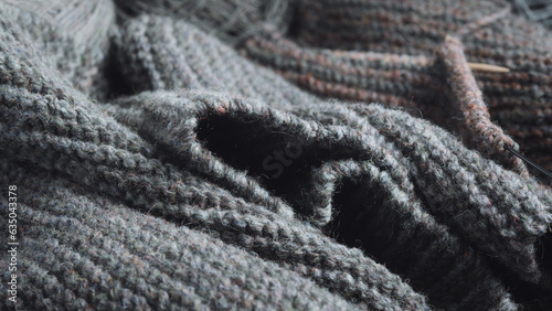 Folds of an unfinished knitted gray scarf and wooden knitting needles.
