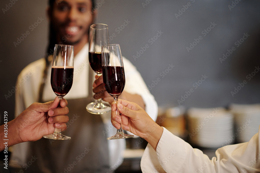 Team of kitchen workers toasting with glasses of wine after finishing long shift