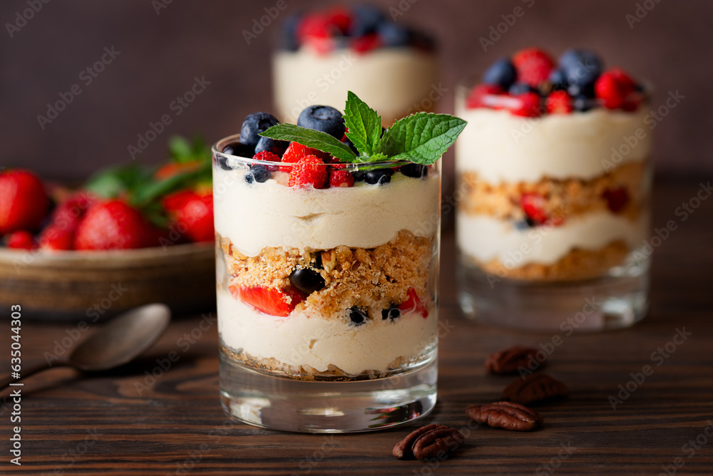 Sweet dessert in a glasses with berries, mint, whipped coconut cream and biscuit on a wooden table. Healthy food, vegan, sugar, gluten and lactose free.