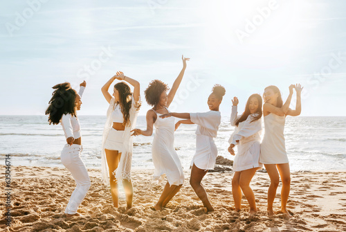 Full length shot of happy multiracial female friends dancing on the beach, having fun, enjoying hen party on ocean shore
