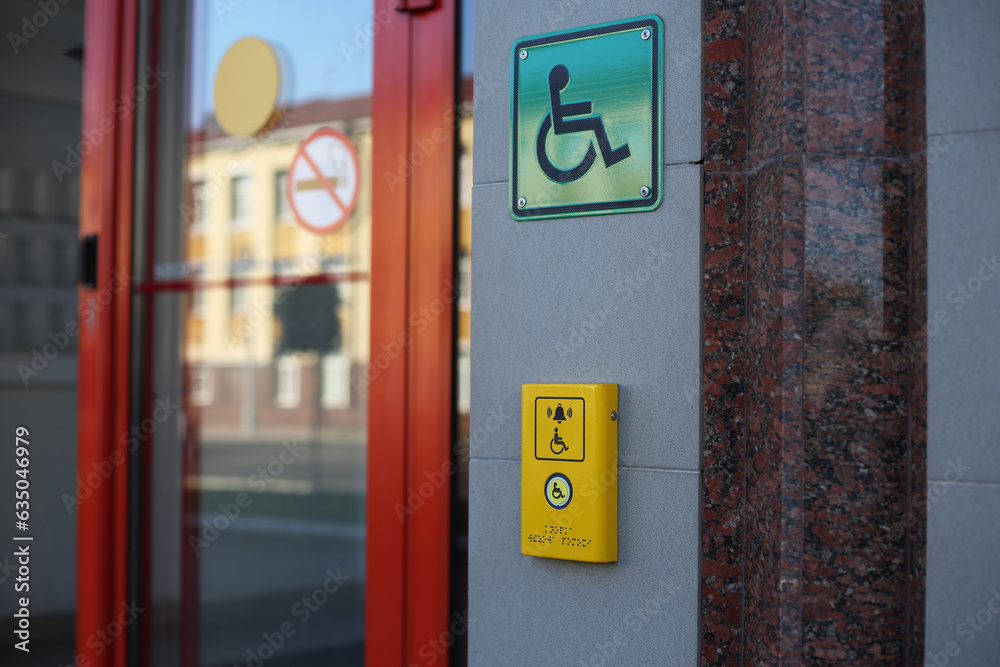 Yellow panel with a call button for help for people with disabilities on a wheelchair to enter the building by stairs. Wheelchair sign on the wall Yellow panel with a call button for help for people with disabilities on a wheelchair to enter the building by stairs. Wheelchair sign on the wall
