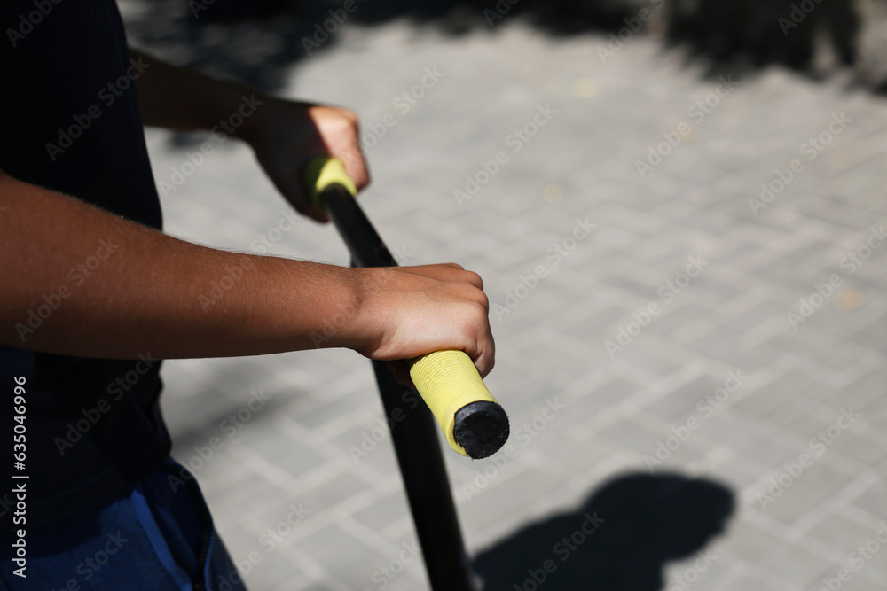 The hands of a young boy hold the steering wheel of a scooter for tricks in a skate park