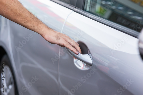 Closeup of a man's hand on the handle of a car opening the door of a gray car in summer. Car rental, sharing automobile, buying a new car, driver, driving lessons
