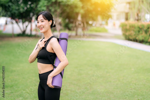Fototapeta Naklejka Na Ścianę i Meble -  Yoga girl. Portrait of young asian slim and healthy girl prepared doing workout in park, standing with rubber mat before exercises on green park at sunset, healthcare and well-being and yoga concept.