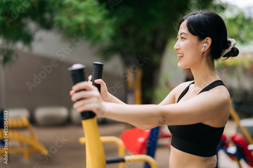 Young asian athletic sportswoman 30s wearing sportswear listening relaxing music while working out exercise equipment outdoor in park. Healthy lifestyle concept