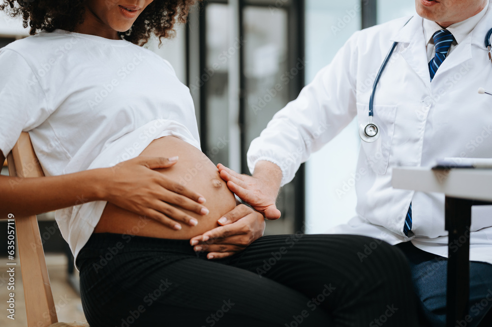 Obraz premium Pregnant african woman has appointment with doctor at clinic. Male gynaecologist OB GYN medic specialist with stethoscope listens to baby's heartbeat in mother's belly. Pregnancy, health care