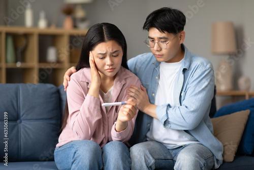 Depressed Korean Couple Holding Negative Pregnancy Test Sitting At Home photo