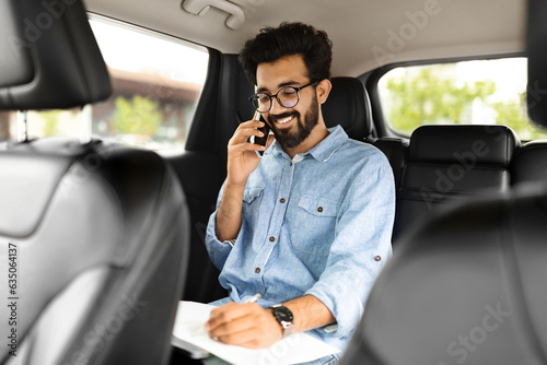 Happy young indian businessman talking over phone, sitting in taxi © Prostock-studio