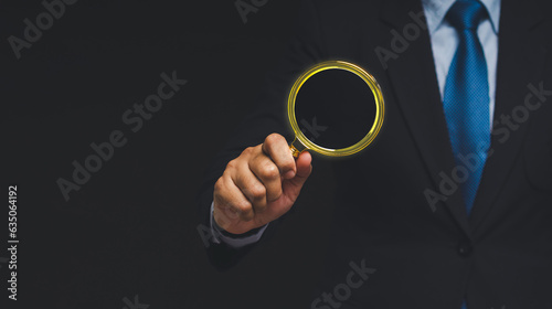 Businessman holding a magnifying glass while standing against a black background.