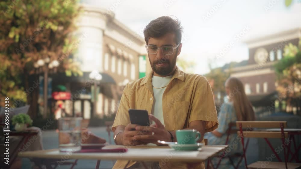 Handsome Multiethnic Man Sitting on a Terrace in a Cafe, Having a Cup of Coffee with Pastry. Happy Indian Man Connecting with Friends Online, Replying to Social Media Posts and Emails on a Smartphone Handsome Multiethnic Man Sitting on a Terrace in a Cafe, Having a Cup of Coffee with Pastry. Happy Indian Man Connecting with Friends Online, Replying to Social Media Posts and Emails on a Smartphone