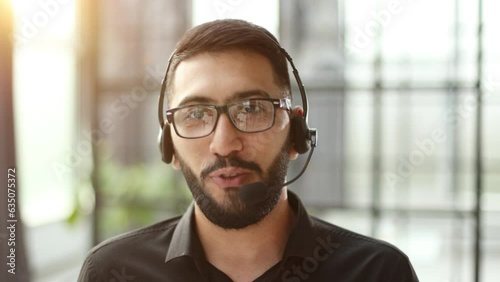 Focused businessman telemarketer telesales agent wear wireless headset make conference video call talk consult online client on computer, male helpline operator work in customer care support office