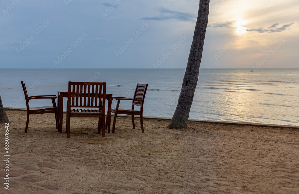 dining table sea view on sand beach with sunset, wood chairs and table