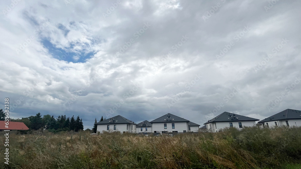 identical white cottages with dark roofs with grass and a sky with rain clouds. village after the rain