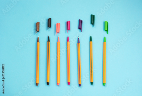 Flat lay top view, orange multi-colored writing pen with caps on a blue background. Stationery, liners for writing pen, pens for design. Colorful markers. Colorful highlighter slim liner 