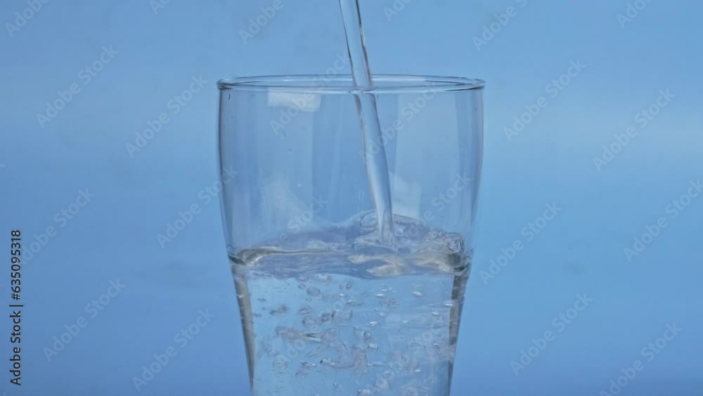 Hand pouring fresh pure water from bottle into glass isolated on blue background, focus on glass. The concept of drinking water. Hand pouring fresh pure water from bottle into glass isolated on blue background, focus on glass. The concept of drinking water.