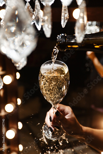 champagne is poured into a glass, and it overflows over the edges pouring over your hands. dark background