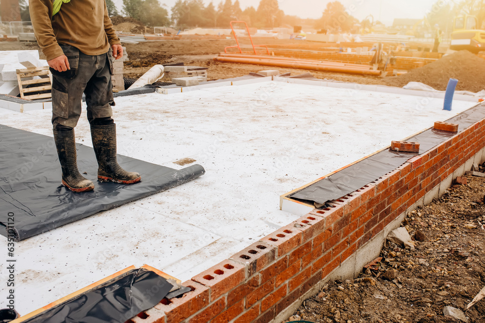 Builder placing polystyrene insulation boards on waterproofing membrane ...