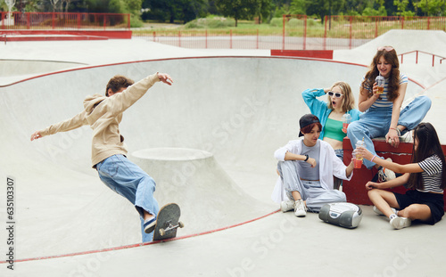 Cheerful friends, teens meeting together at skateboard park, having fun, riding on skate, talking. Boy doing stunts. Concept of youth culture, sport, dynamic, extreme, hobby, action and motions