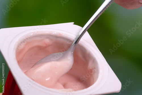 Close-up of a teaspoon with pink yogurt in a cup, macro photography