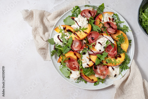 Healthy summer salad with peach, burrata, arugula and jamon
