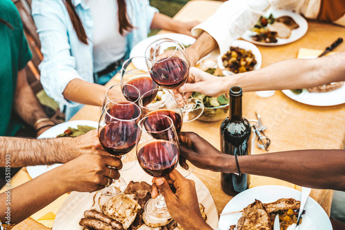 People clinking red wine glasses on rooftop dinner party - Happy friends eating meat and drinking wineglass at restaurant patio - Food and beverage lifestyle concept with guys and girls dining outdoor