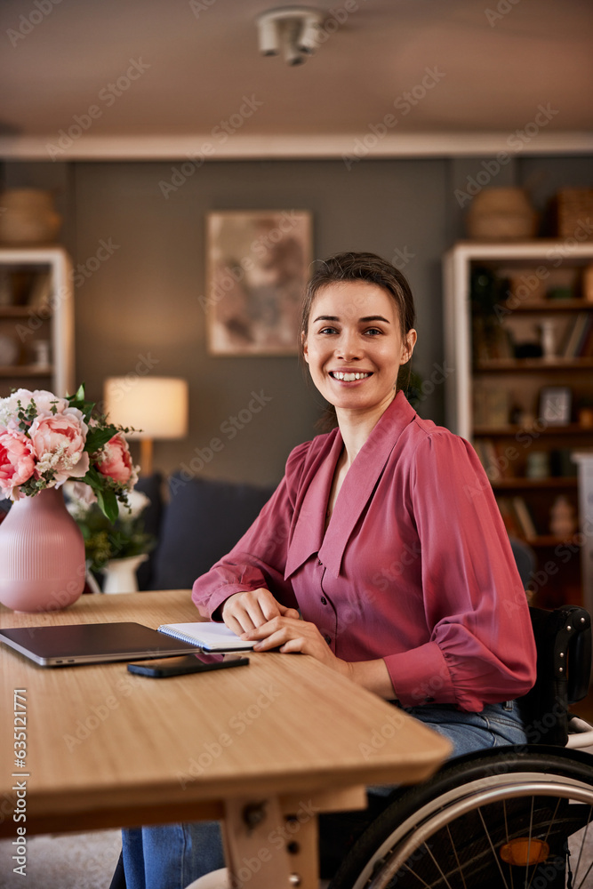 Fototapeta premium Portrait of a cheerful female freelancer with a disability typing on a laptop.