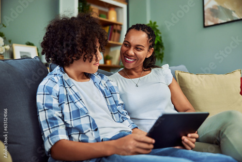 A smiling African mother sitting with her teenage son with a tablet on the couch.