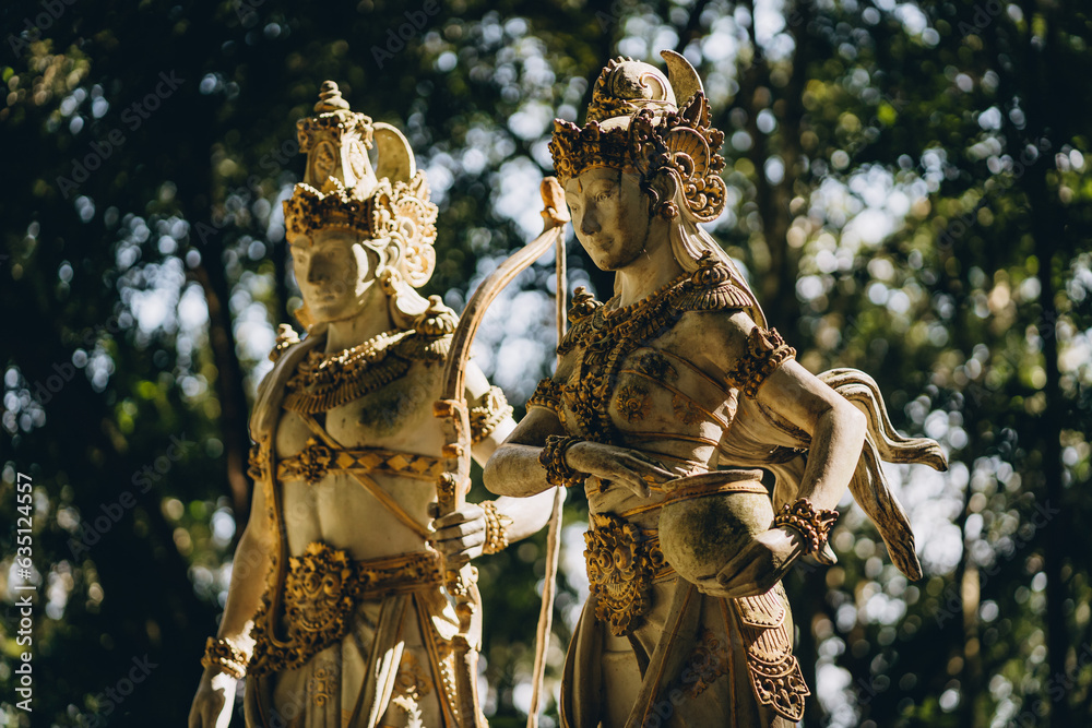 Fototapeta premium Close up shot of golden balinese statues with green nature background. Traditional indonesian architecture with hindu decoration details