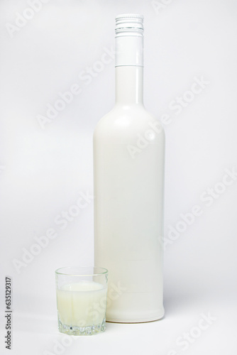A glass of white liquor next to a bottle on a white background. Dessert alcoholic drink