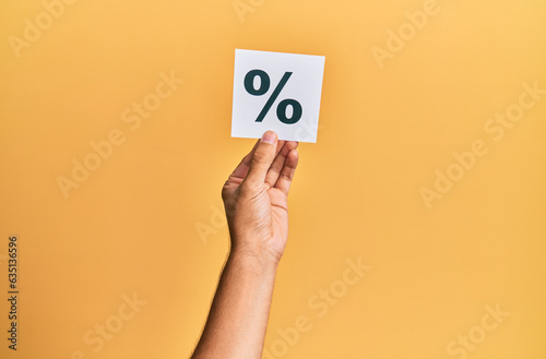 Hand of caucasian man holding paper with percentage mark over isolated yellow background