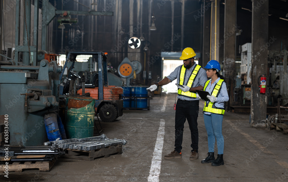African American male and female engineers in safety vest and helmet working at heavy metal industrial factory. Two technician foreman discussing for checking and repairing machine at factory. African American male and female engineers in safety vest and helmet working at heavy metal industrial factory. Two technician foreman discussing for checking and repairing machine at factory.
