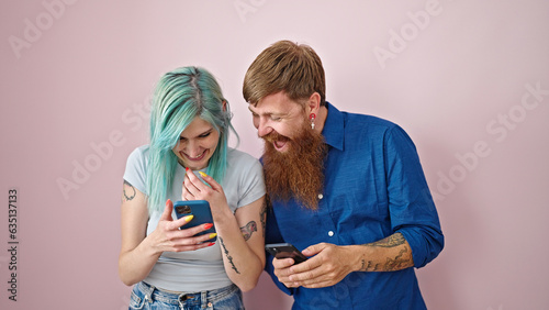 Man and woman couple using smartphones smiling over isolated pink background