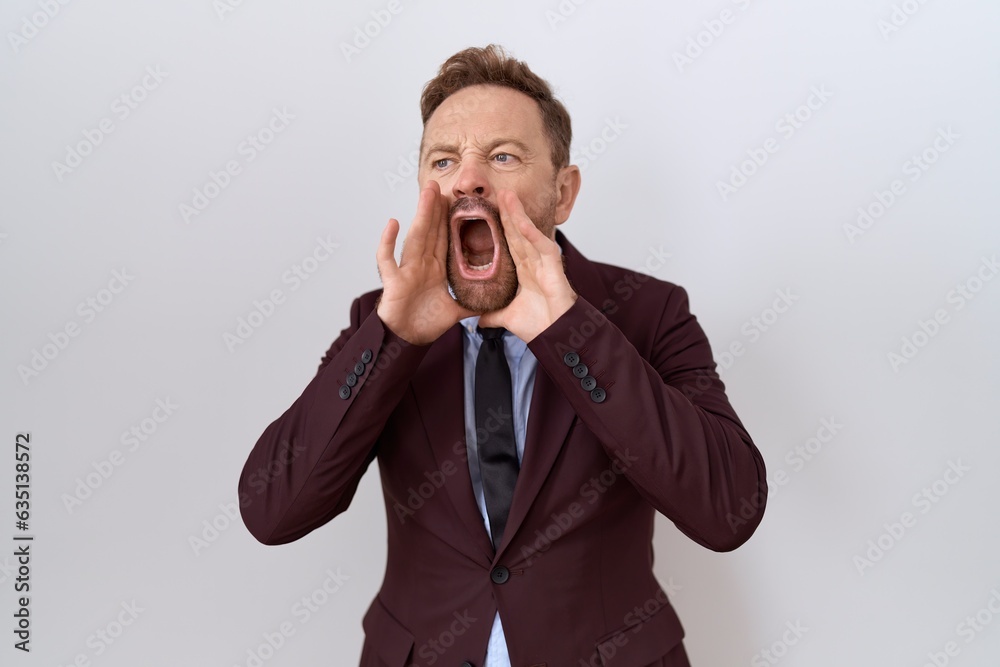 Middle age business man with beard wearing suit and tie shouting angry out loud with hands over mouth Middle age business man with beard wearing suit and tie shouting angry out loud with hands over mouth