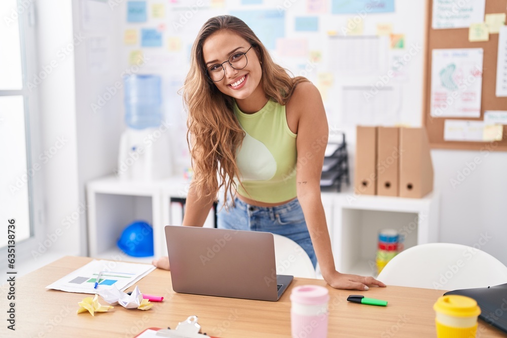 Young beautiful hispanic woman business worker smiling confident standing by desk at office