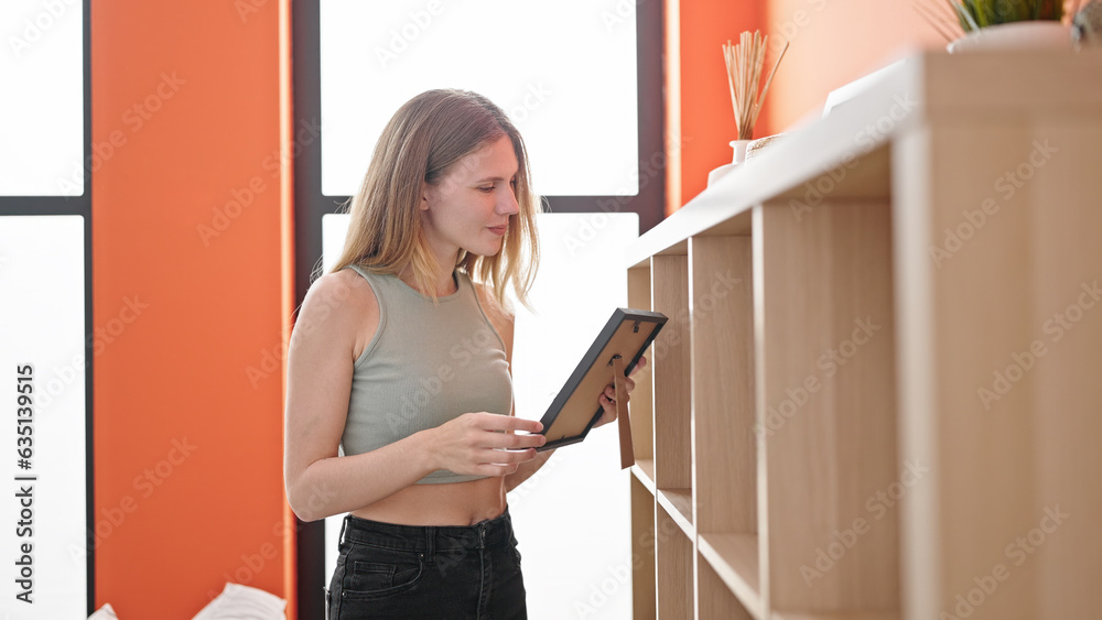 Young blonde woman organizing shelving holding photo at home