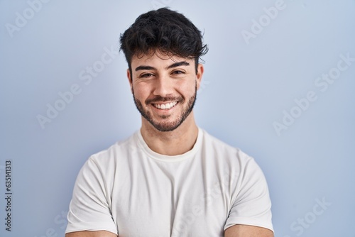 Hispanic man with beard standing over white background happy face smiling with crossed arms looking at the camera. positive person.