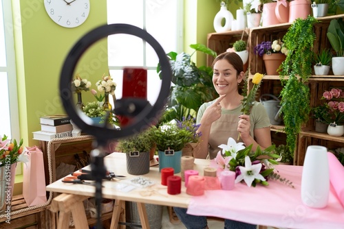Beautiful brunette woman working at florist shop recording tutorial with smartphone smiling happy pointing with hand and finger