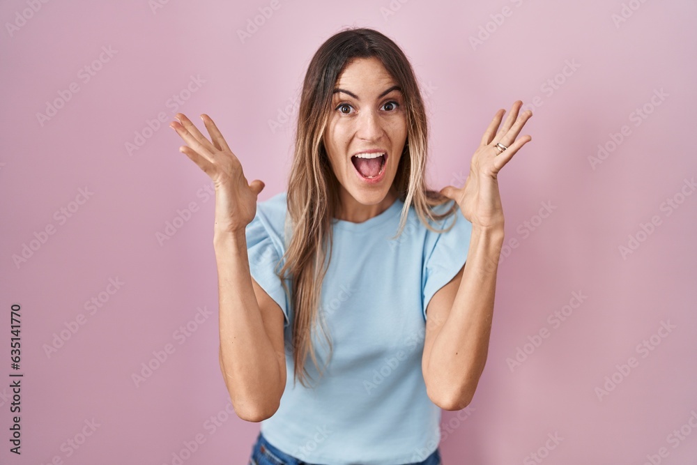 Young hispanic woman standing over pink background celebrating crazy and amazed for success with arms raised and open eyes screaming excited. winner concept Young hispanic woman standing over pink background celebrating crazy and amazed for success with arms raised and open eyes screaming excited. winner concept