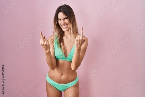 Quadro su tela Young hispanic woman wearing bikini over pink background showing middle finger doing fuck you bad expression, provocation and rude attitude